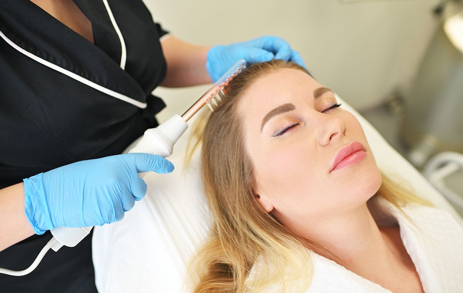 Woman receiving high frequency hair treatment; technician holds wand to her scalp.